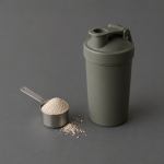 Scoopje poeder met maatschepje en onbedrukte shaker op een antracietkleurige achtergrond